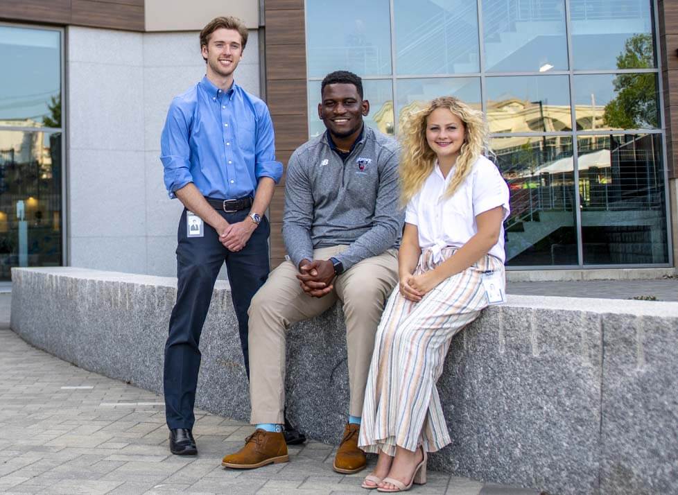 A photo of three UMaine management students outside Bangor Savings Bank