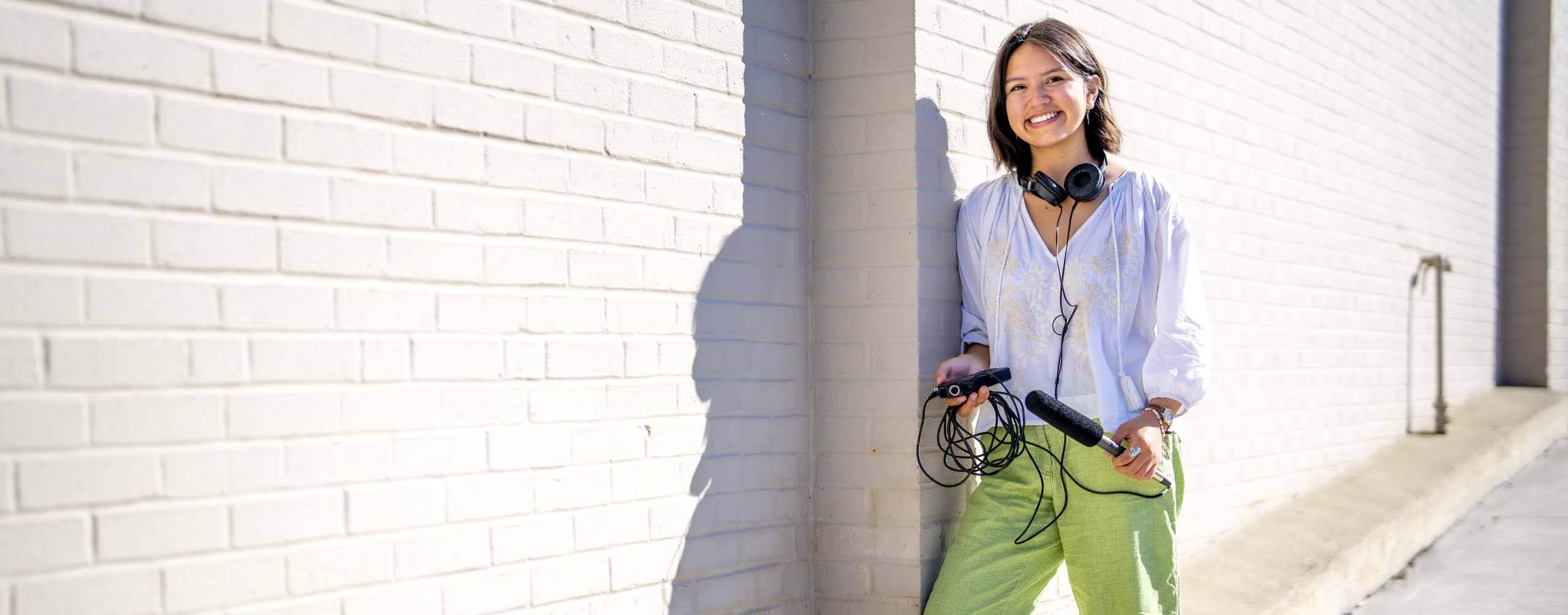 A photo of a student standing outside holding a microphone and headphones