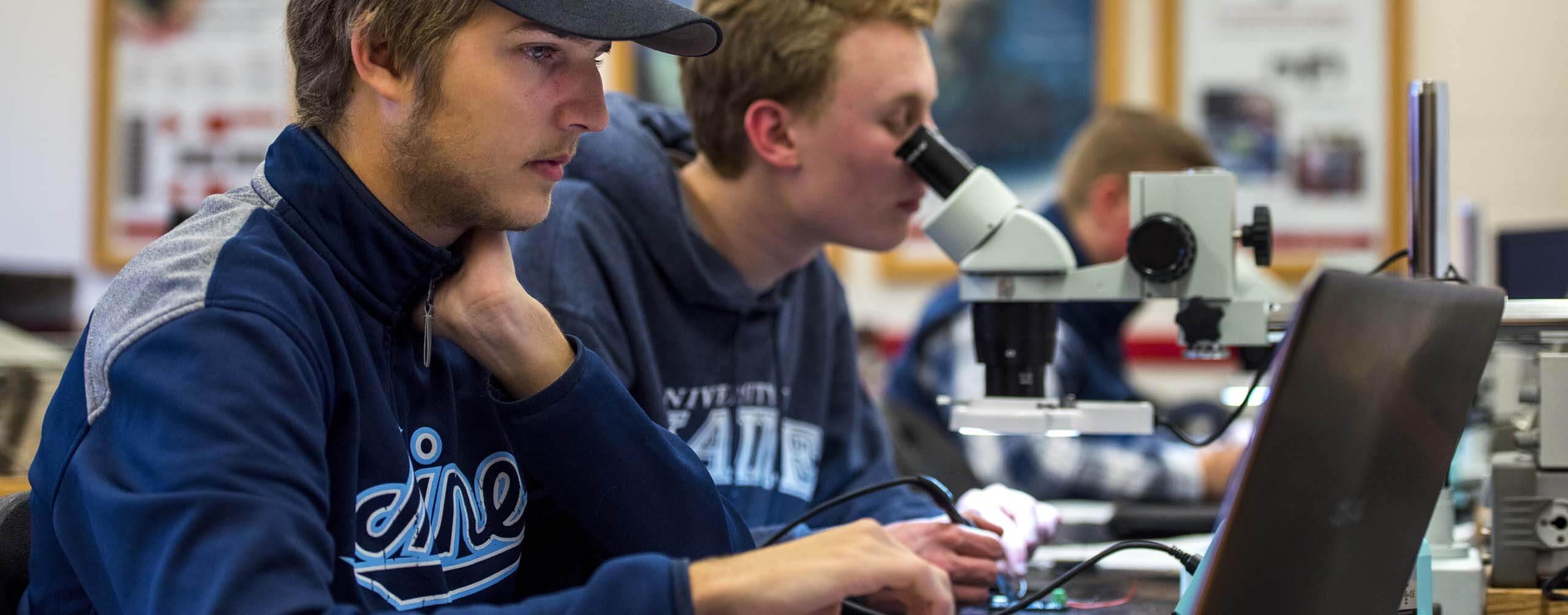 A photo of two people, one is looking through a microscope