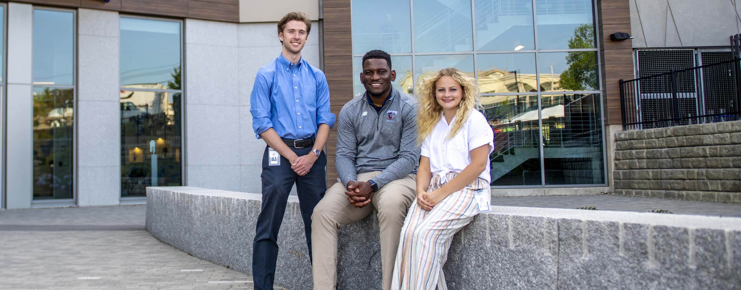 A photo of three UMaine management students outside Bangor Savings Bank