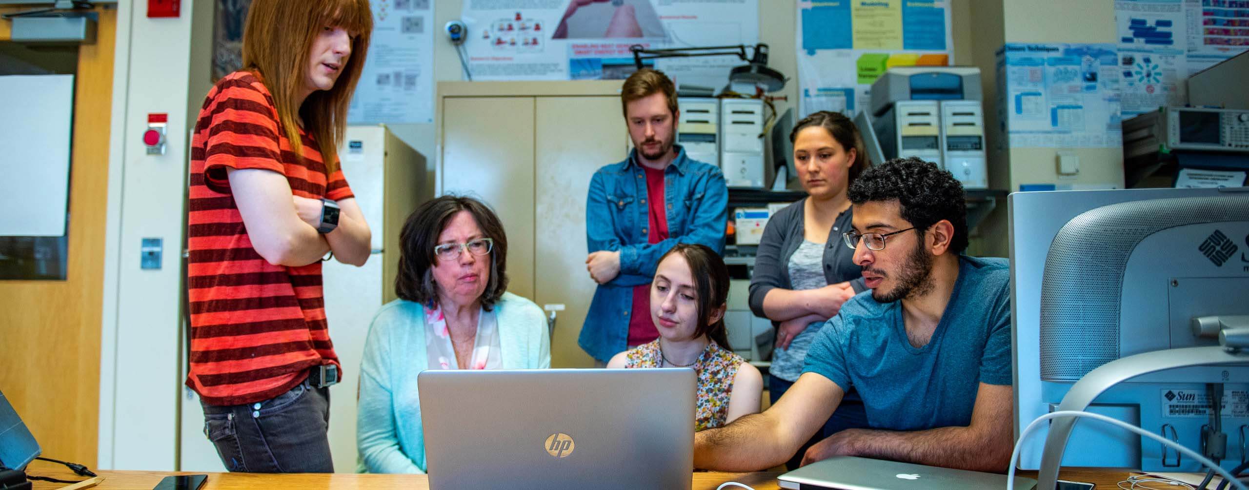 A photo of a group of students looking at a laptop