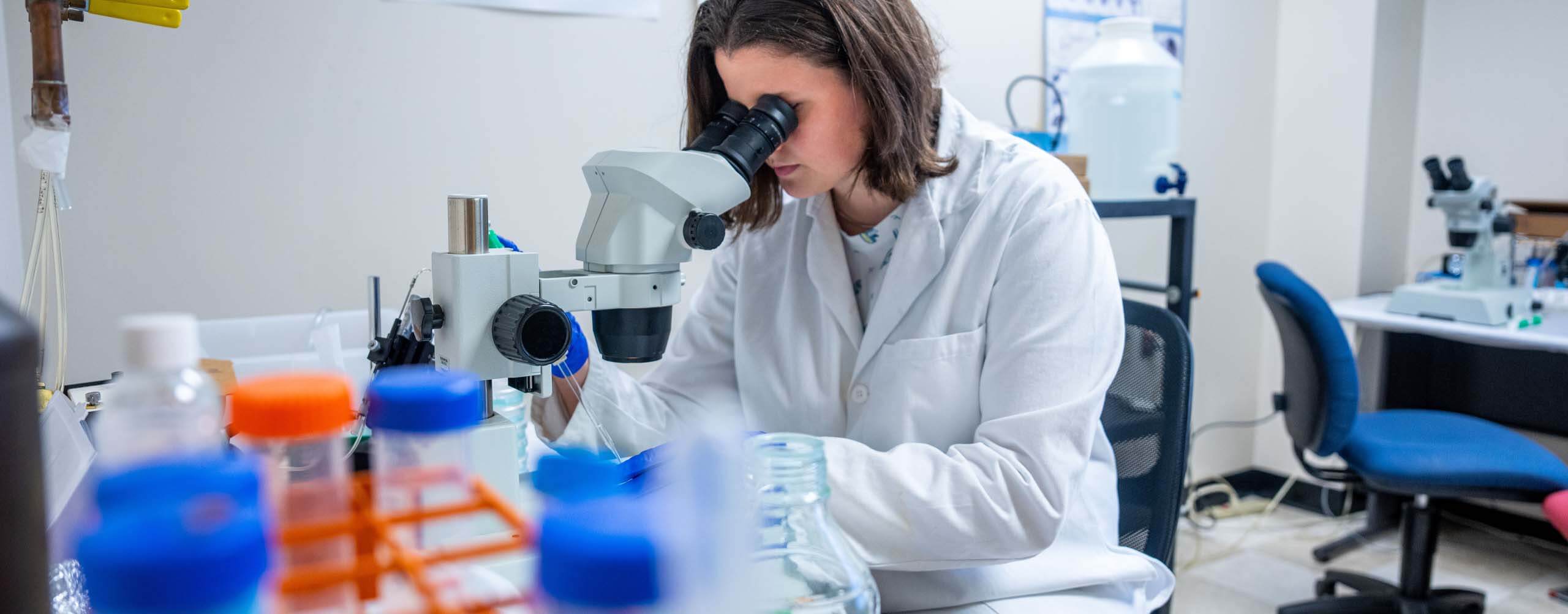 A photo of a person looking into a microscope
